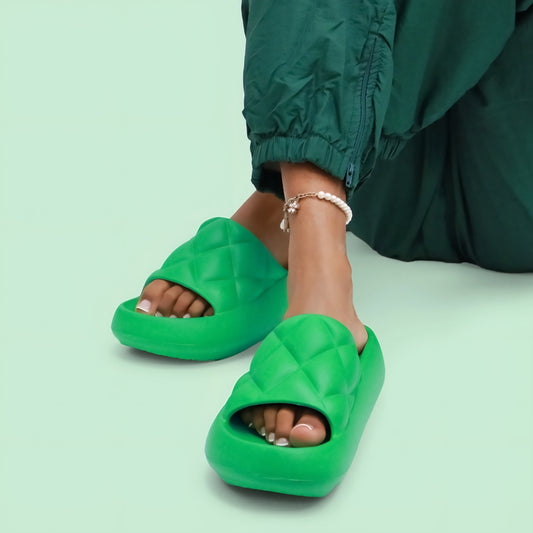 Green quilted slide sandals worn with green pants on a light green background