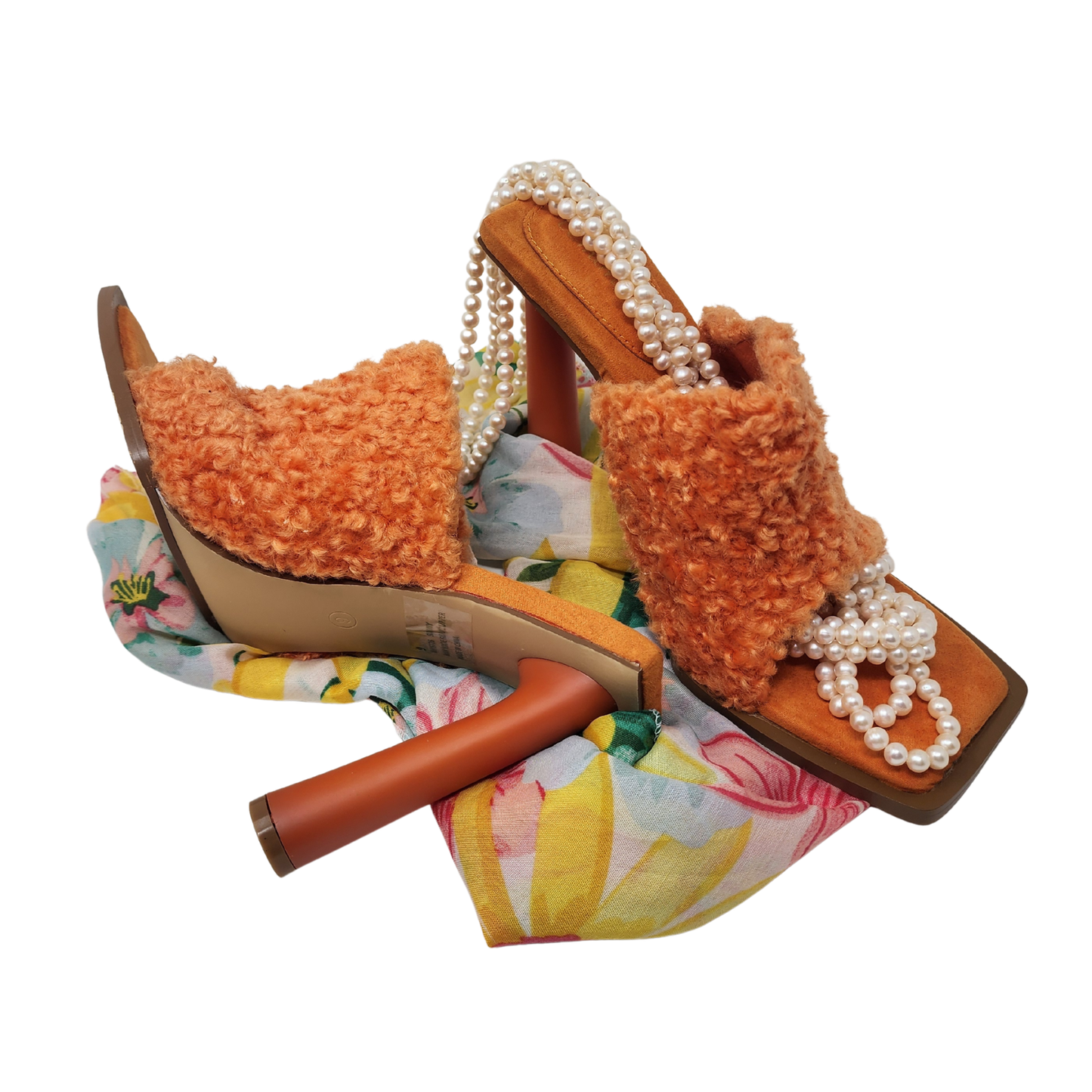 Orange fuzzy sandals with pearl straps on a floral background